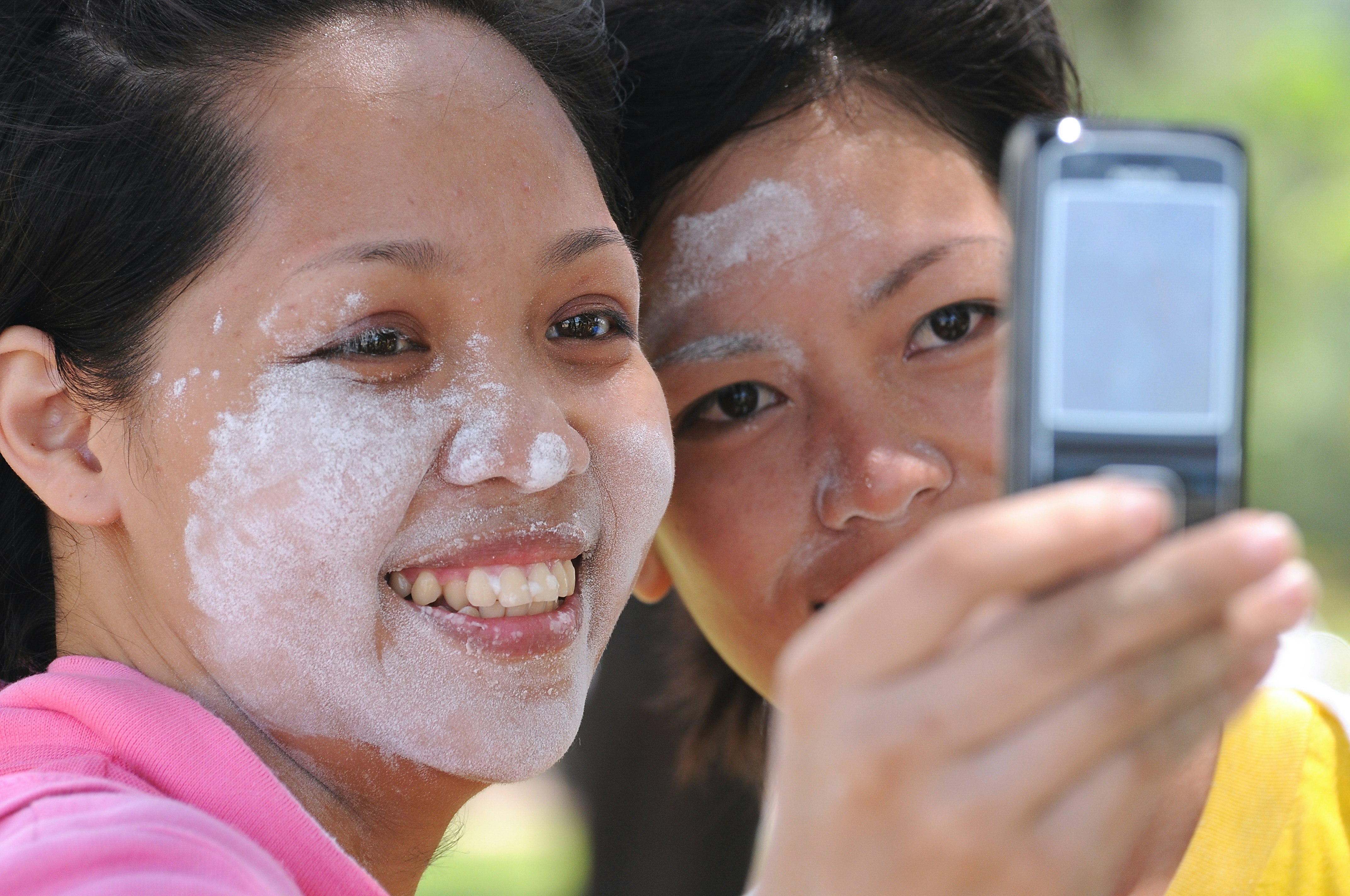Two women take a selfie, faces with white substance